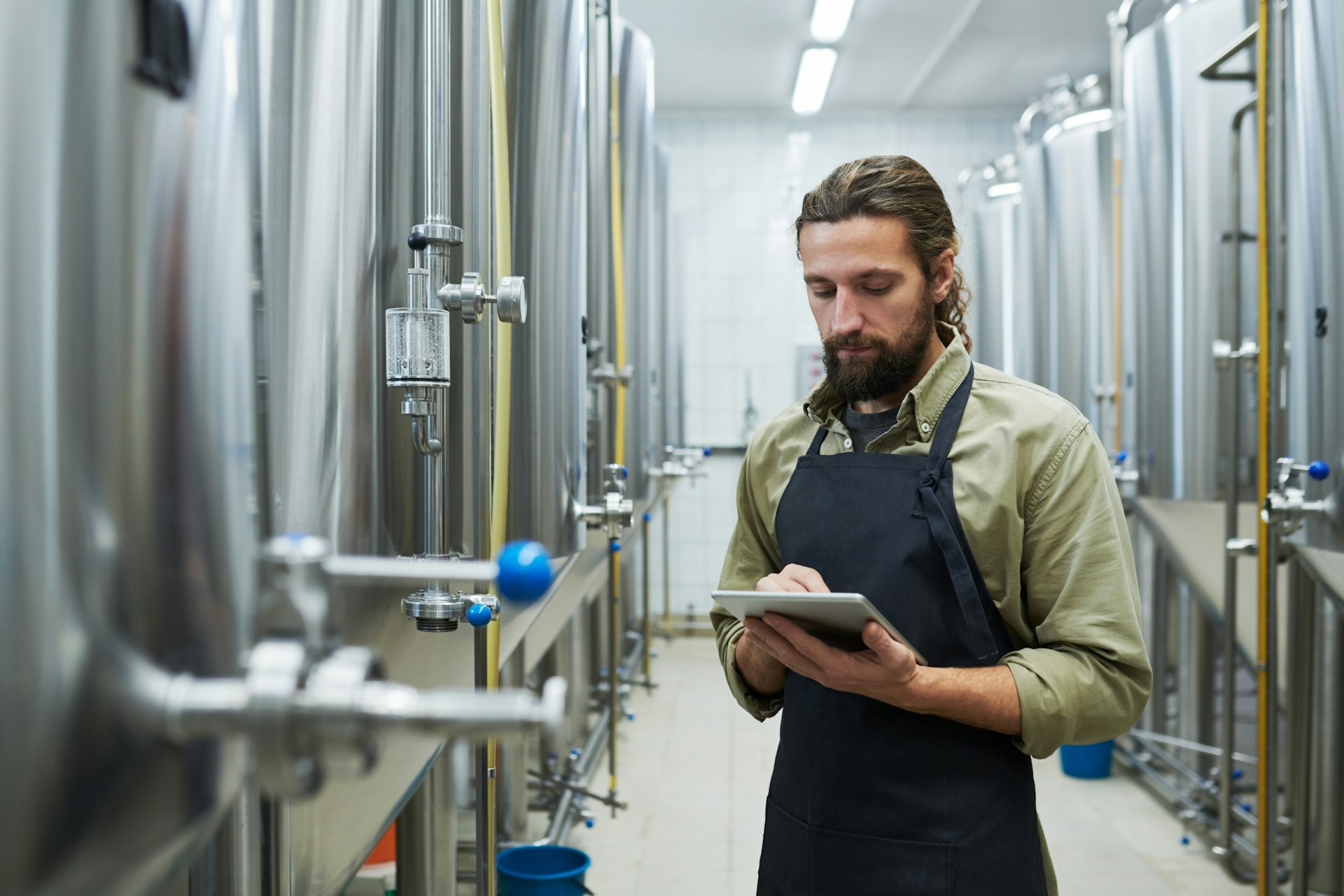Brewery worker checking a tablet between stainless steel tanks